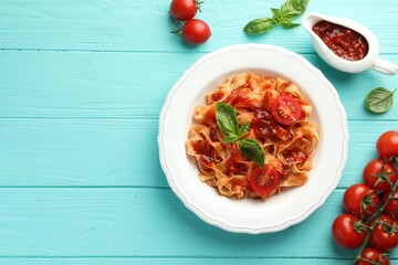 Delicious pasta with tomato sauce and basil on turquoise wooden table, flat lay. Space for text