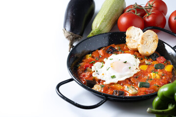 Vegetable pisto manchego with tomatoes, zucchini, peppers, onions,eggplant and egg, served in frying pan isolated on white background
