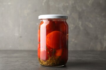Tasty pickled tomatoes in jar on grey table