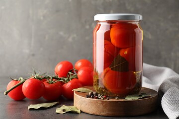 Tasty pickled tomatoes in jar, spices and fresh vegetables on grey table. Space for text