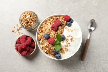 Tasty granola with berries and yogurt served on grey textured table, flat lay
