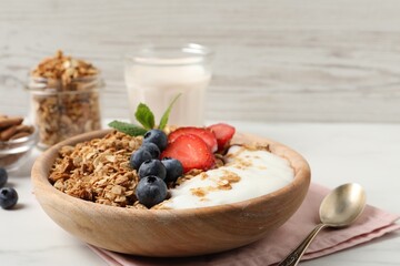 Tasty granola with berries and yogurt in bowl on white table, closeup