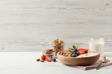 Tasty granola with berries and yogurt in bowl on white marble table. Space for text