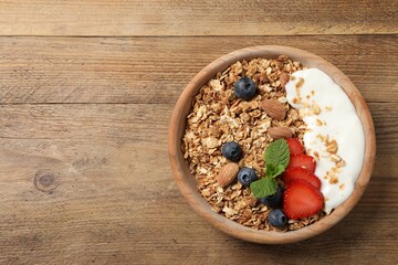 Tasty granola with berries, almond and yogurt in bowl on wooden table, top view. Space for text
