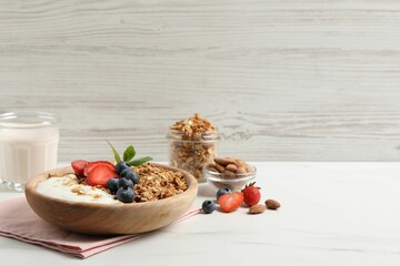 Tasty granola with berries and yogurt in bowl on white marble table. Space for text