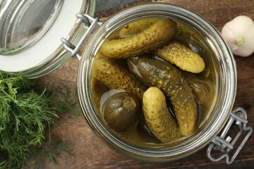 Pickled cucumbers in jar, garlic and dill on wooden table, flat lay