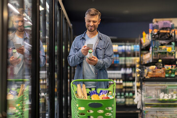 Positive man scanning bar code on product through cellphone, choosing dairy products in supermarket