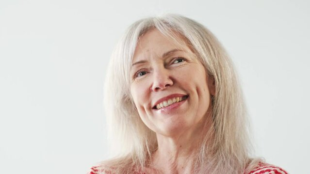 Portrait of Caucasian middle aged grandmother joyfully glancing at camera in light white studio. Having good feelings. Positive female looking directly at camera. Concept of happy woman.