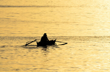 A lone fisherman in a small boat photographed during the golden hour.