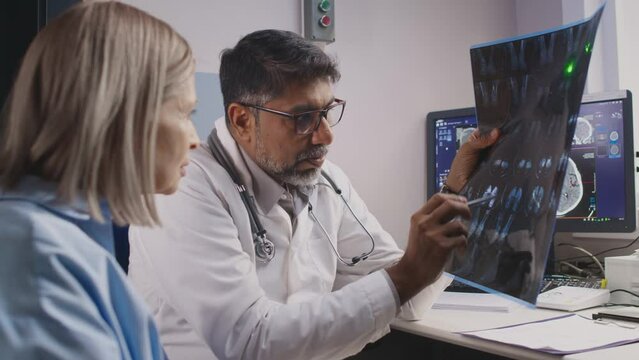 Medium slowmo shot of middle-aged Caucasian woman sitting near orthopedist in clinic looking at feet X-Ray film scan, listening to doctors advice and recommendations