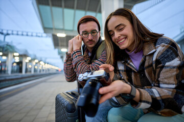 A young couple immersed in conversation while reviewing photos on a camera, enjoying a relaxed...
