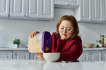 A little girl with Down syndrome pours cereal into a bowl at her kitchen table.
