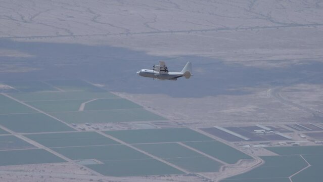 Cinematic zoom out on c-130 airplane soaring over fields