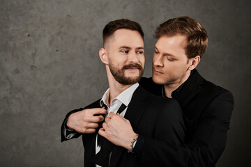 Two men in elegant suits share a tender moment in a studio portrait.