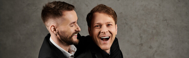 Fototapeta premium Two men in suits laugh together against a textured concrete wall.