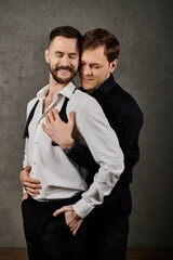 Two men in dapper suits embrace lovingly in a studio setting.