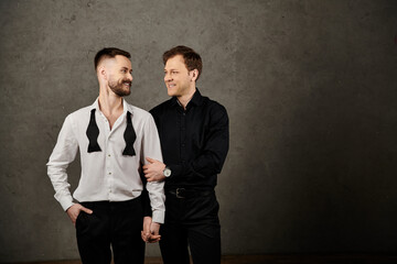 Two men in elegant suits, standing close and looking lovingly at each other.