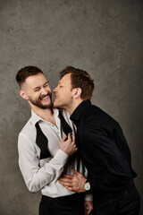 Two men in elegant suits, one holding the other close as they share a tender moment.