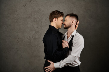 A gay couple in elegant suits stand close, sharing a tender moment.