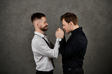 Two men in stylish suits share a tender moment, their hands clasped together.