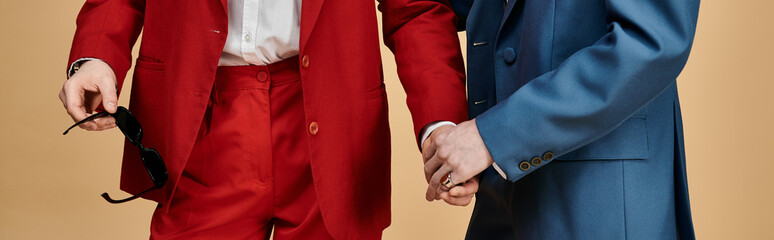 Two men in elegant suits hold hands, displaying a loving connection.