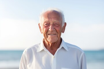 Portrait of a grinning man in his 80s wearing a simple cotton shirt over bare concrete or plaster wall