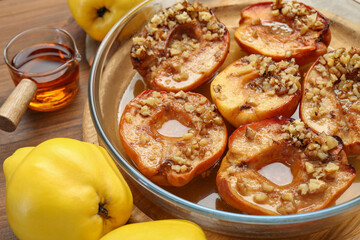 Tasty baked quinces with walnuts and honey in bowl on wooden table, closeup