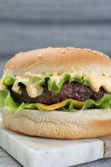 Delicious cheeseburger with lettuce, sauce and patty on table, closeup