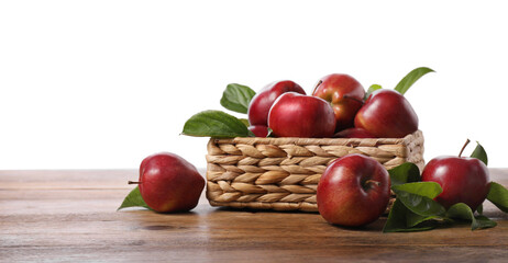 Fresh red apples and leaves in basket on wooden table against white background. Space for text