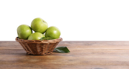 Ripe green apples in wicker basket on wooden table against white background. Space for text