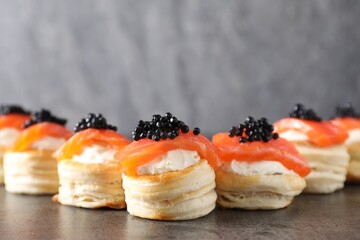 Delicious puff pastry with cream cheese, salmon and black caviar on grey table