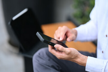 Young businessman typing text message on mobile phone while sitting outside office building