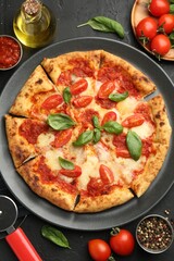 Delicious Margherita pizza, ingredients and cutter on black table, top view