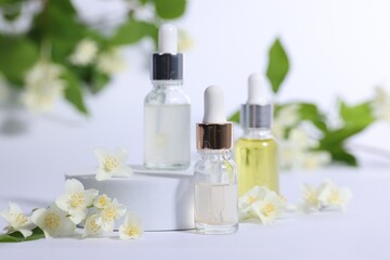 Presentation of essential oils in bottles and beautiful jasmine flowers on white background, closeup