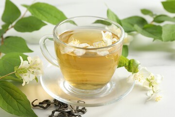 Aromatic jasmine tea in cup, flowers and leaves on white table