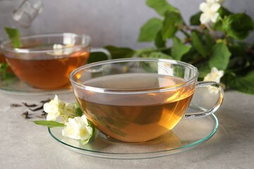 Aromatic jasmine tea in cups, flowers and green leaves on light grey table