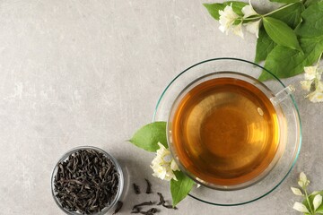 Aromatic jasmine tea in cup, flowers and dry leaves on light grey table, flat lay. Space for text