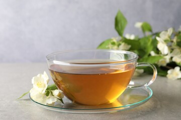 Aromatic jasmine tea in cup, flowers and green leaves on light grey table