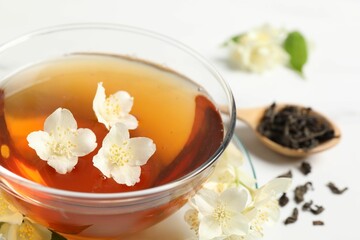 Hot jasmine tea in cup and flowers on white marble table, closeup