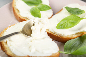 Delicious sandwiches with cream cheese and basil leaves on plate, closeup