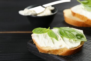 Piece of bread with cream cheese and basil on black wooden table, closeup. Space for text