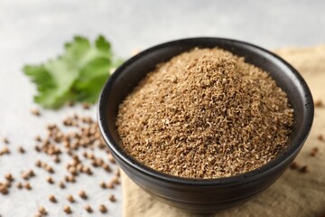 Coriander powder in bowl and seeds on table, closeup