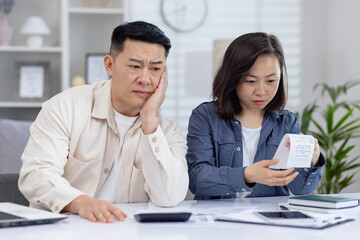 Obraz premium A concerned couple is reviewing their finances at home, looking over bills and documents. They appear stressed and absorbed in the task.