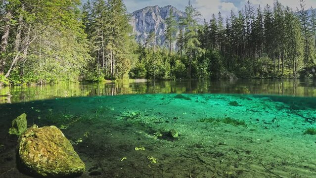 Half underwater dome shot of Green Lake - Gruner See - in Austria. Camera plunges into the water of lake with green bottom, Alps mountains in the background