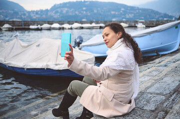 Woman taking a selfie near boats at a scenic lakeside location