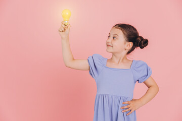 Cute smiling little girl holding glowing light bulb on pink background with copy space