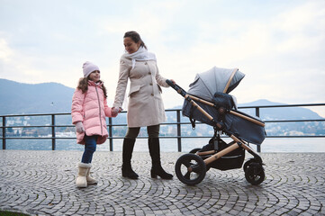 Mother and daughter walking with stroller along lakeside promenade on a winter day