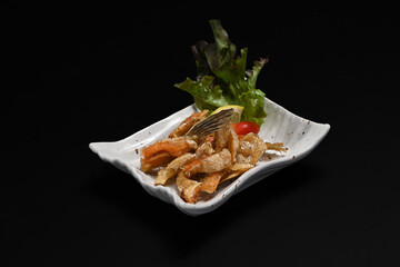 Delicious fried salmon belly in white ceramic plate isolate on black background. Appetizer and Japanese food concept