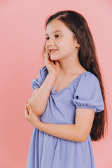 Сute happy little girl in blue dress posing in studio with pink background