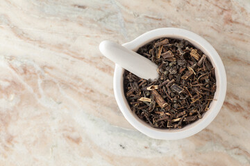 Top-view of Dry Organic Bhringraj (Eclipta prostrata) leaves, in white ceramic mortar and pestle, on a marble background.